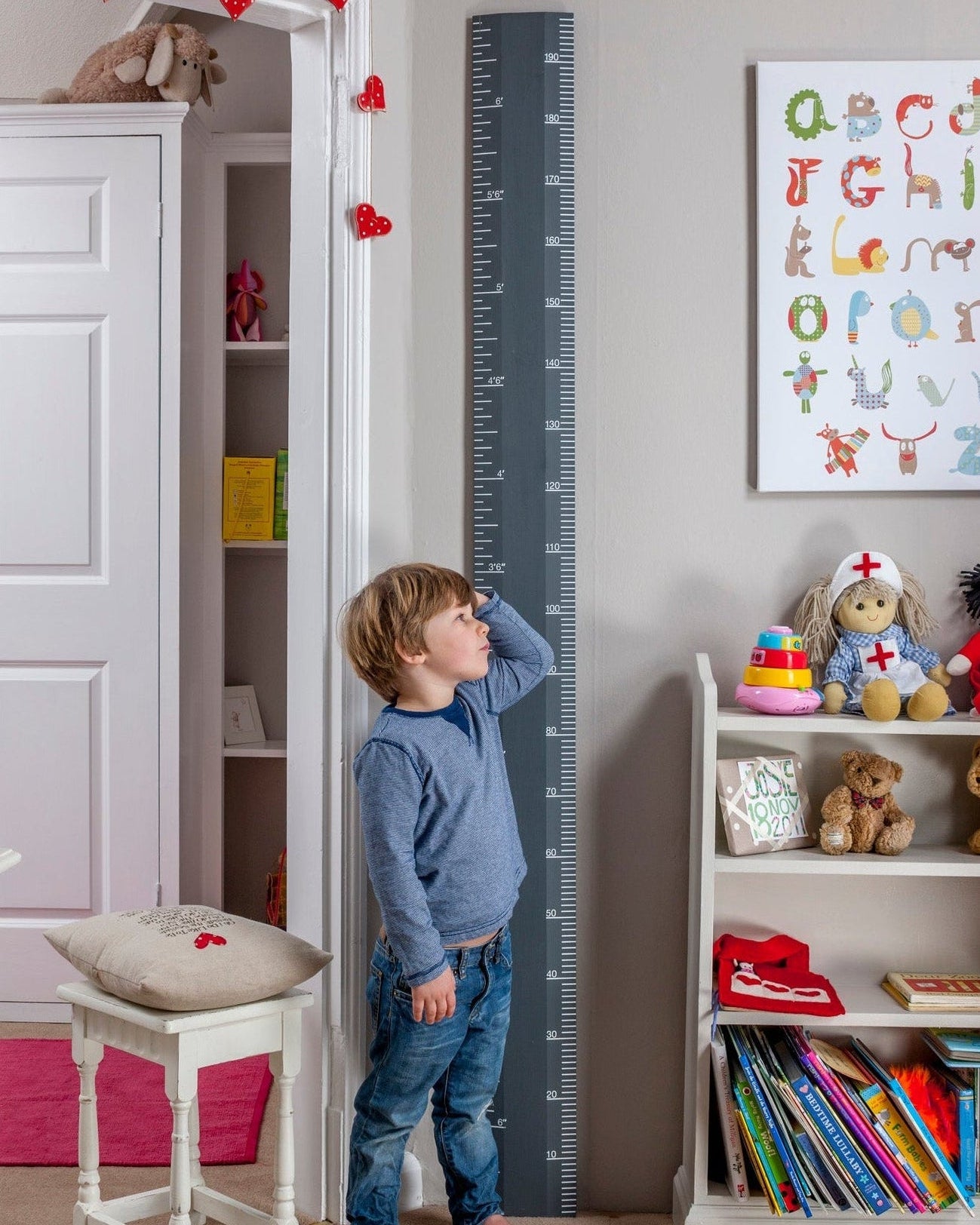 Child standing in a room with a growth chart, books, and toys.