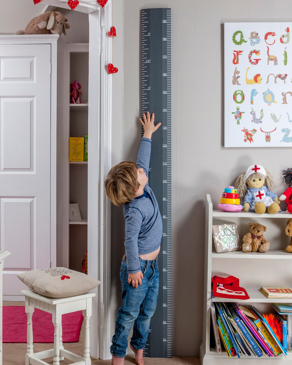 Child measuring height against a growth chart in a child's room with books and toys.