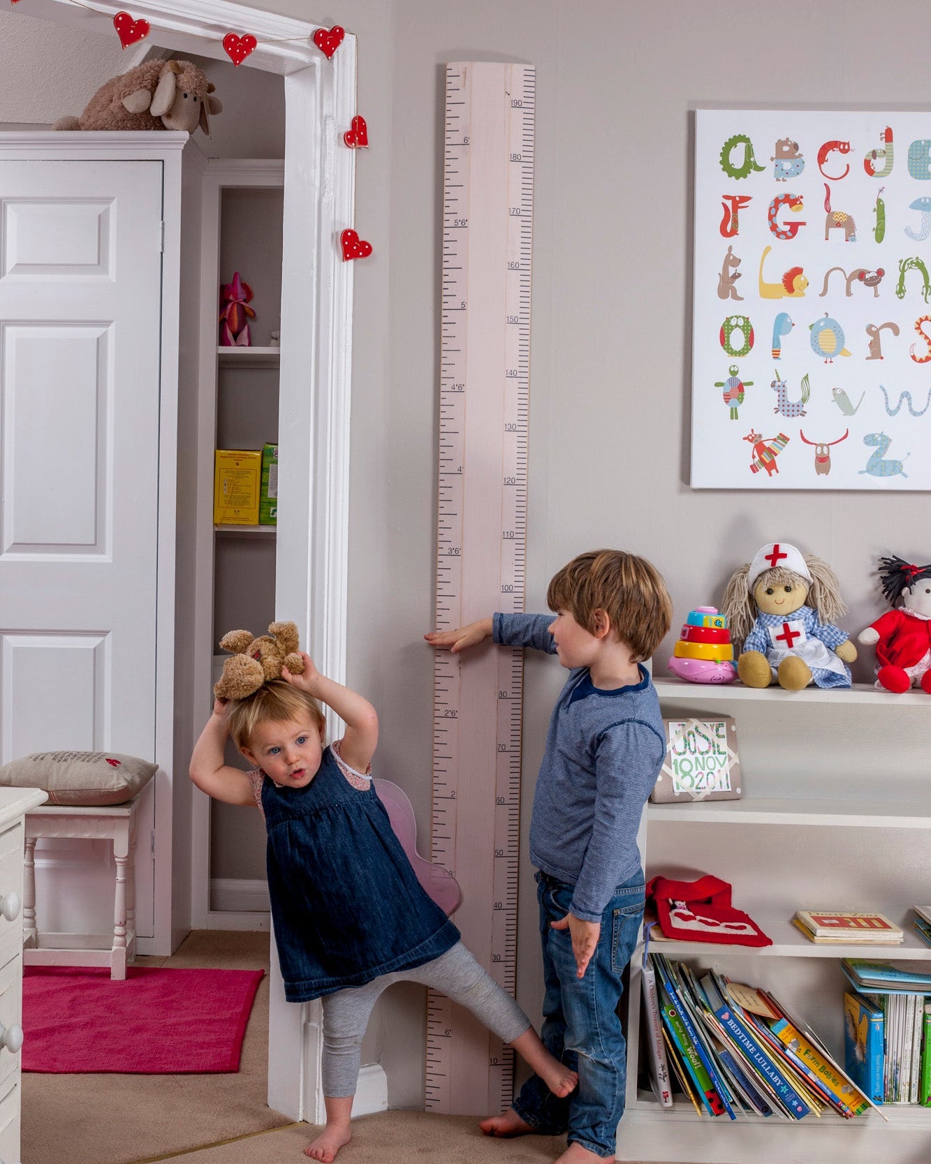 Children playing near a growth chart in a child's room with toys and books.