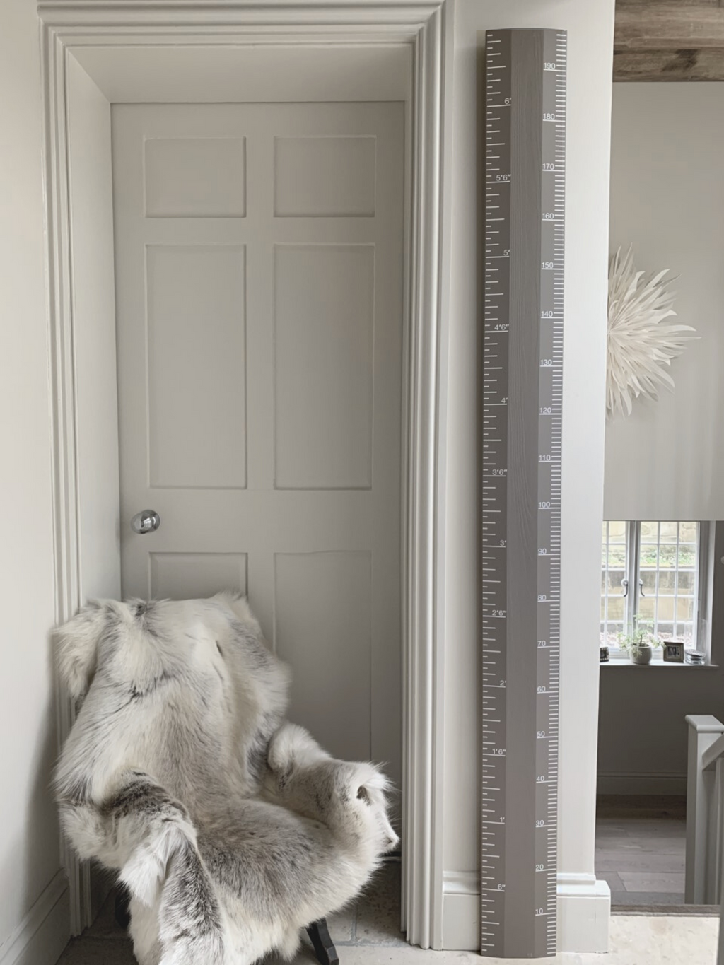 Gray door with a fur throw and a tall decorative ruler against a white wall.