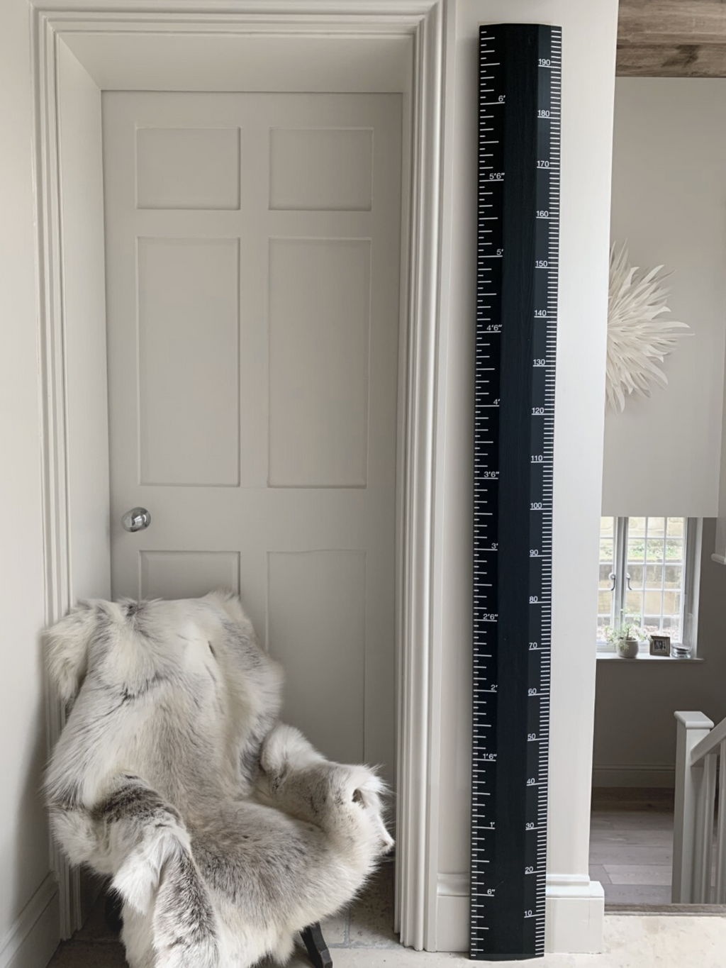 Black growth chart against a white wall next to a door with a fur throw on a chair.