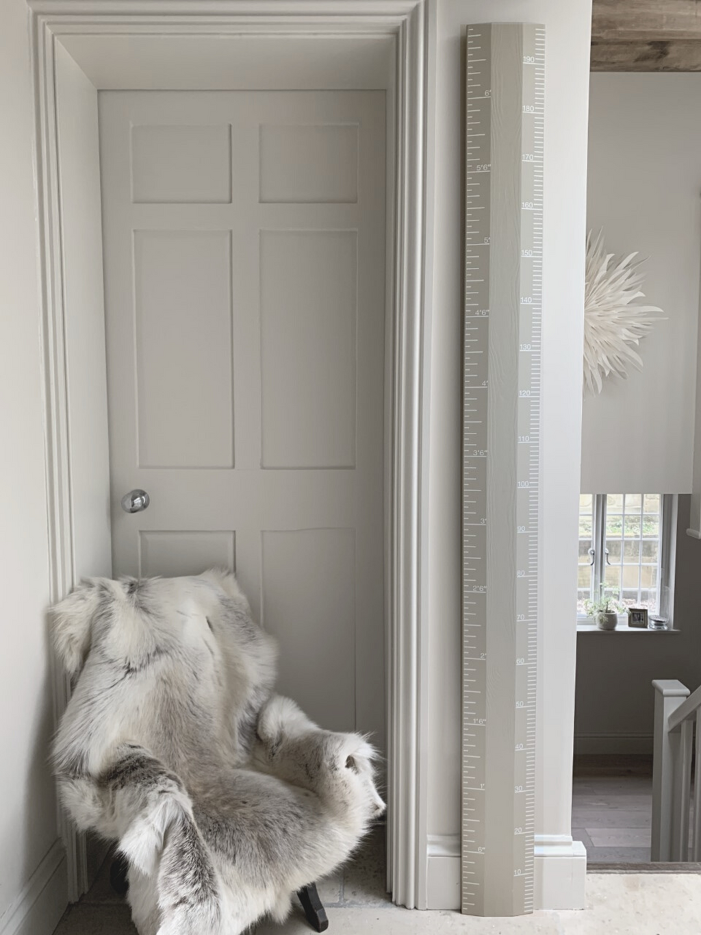 Gray door with a fur throw draped over a chair in a room with a tall mirror.