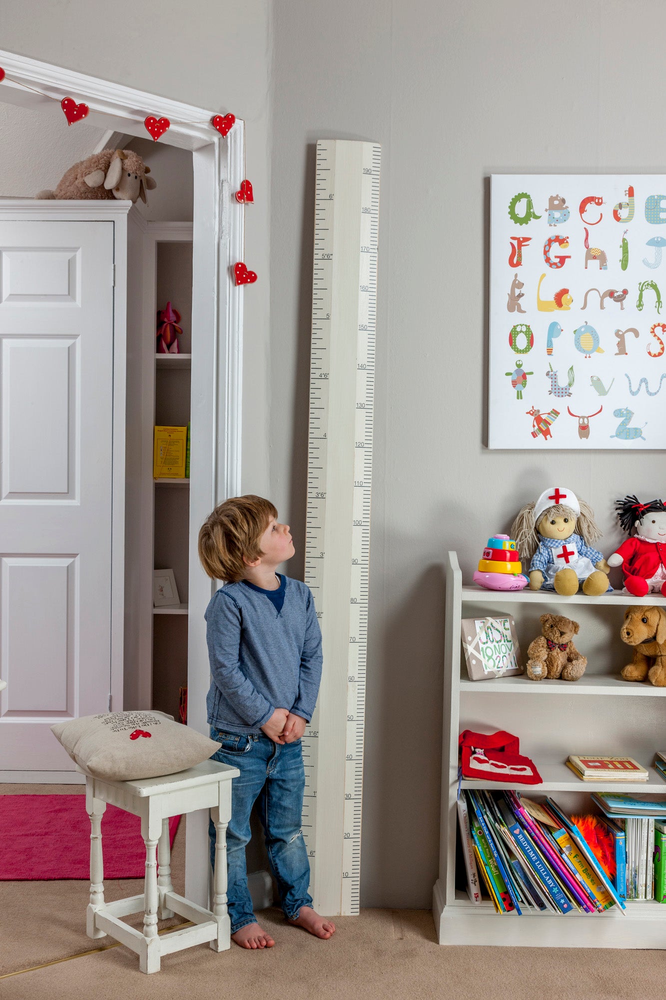 Child standing next to a growth chart in a room with toys and books.